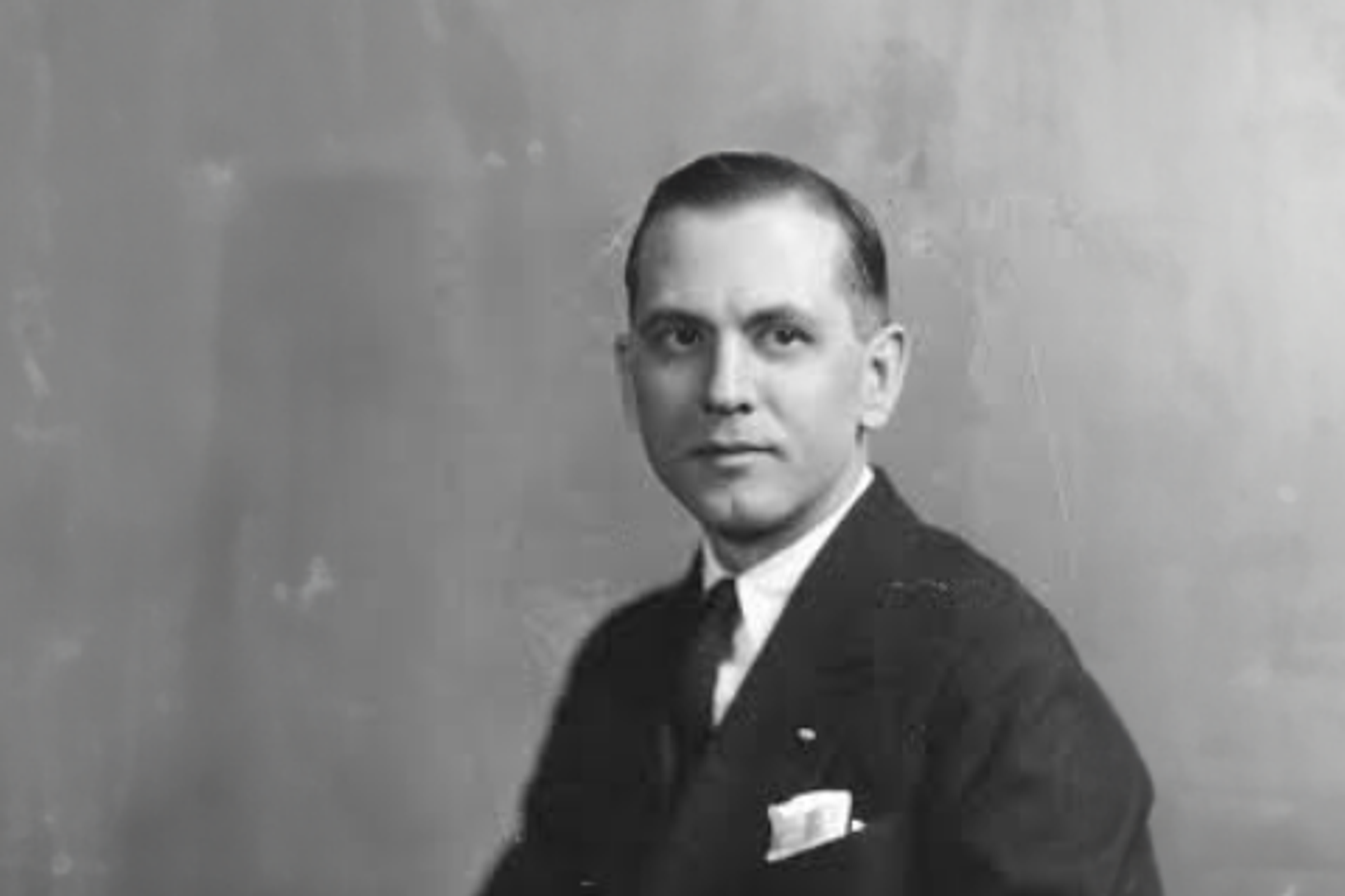 Black-and-white portrait of a man in a suit in front of a wall