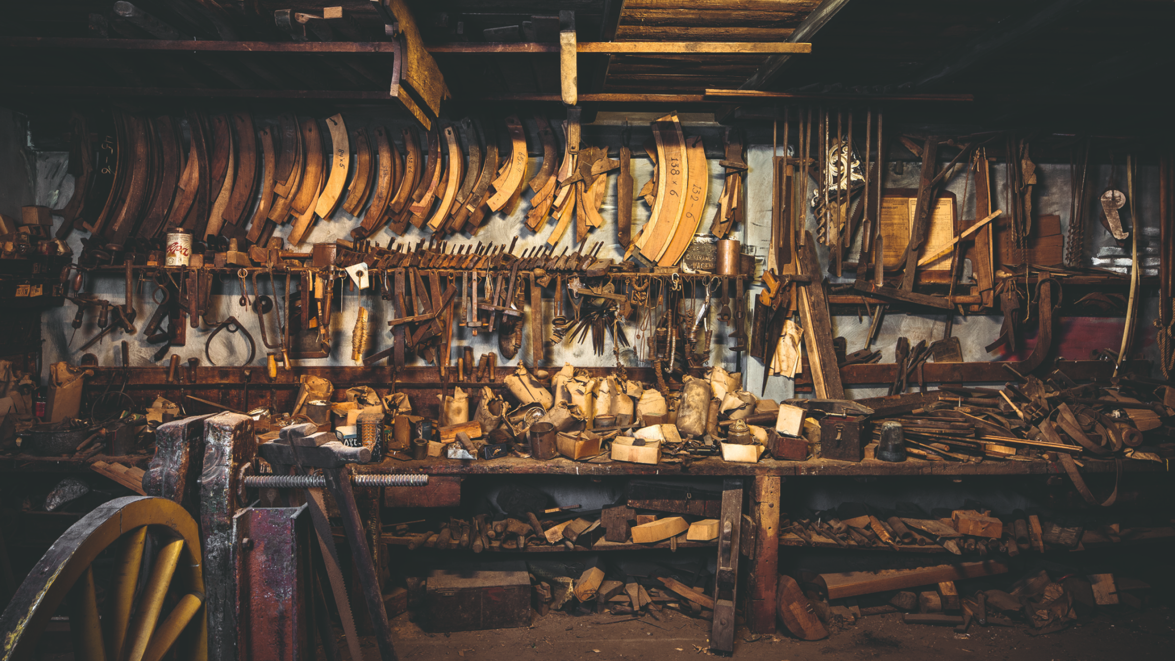Oud gereedschap aan een lange muur boven een houten werkbank