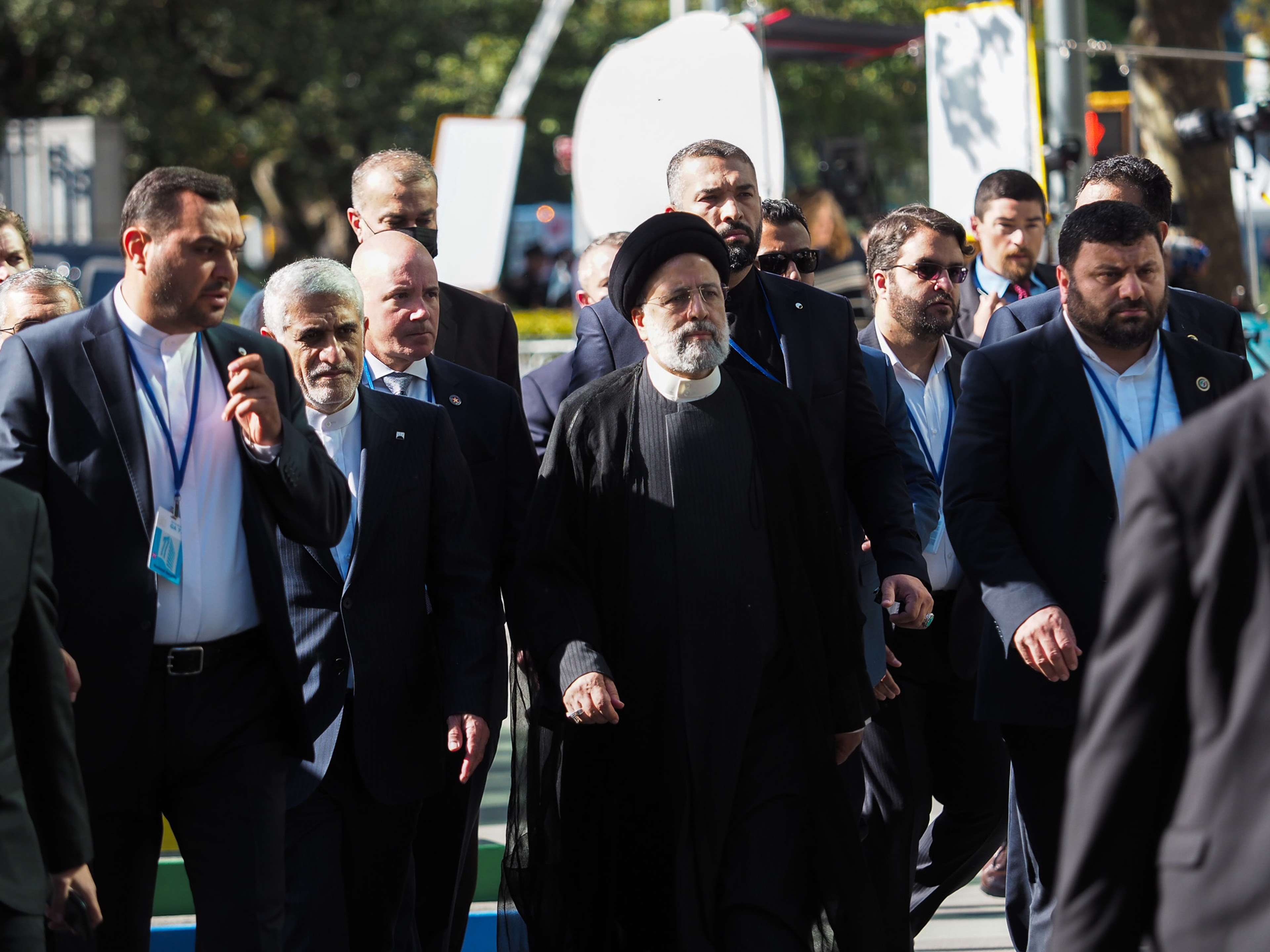 Iranian President Ebrahim Raisi in a black clerical robe and black turban walking through a tight phalanx of security and aides in suits wearing UNGA badges on blue lanyards, on a New York street.