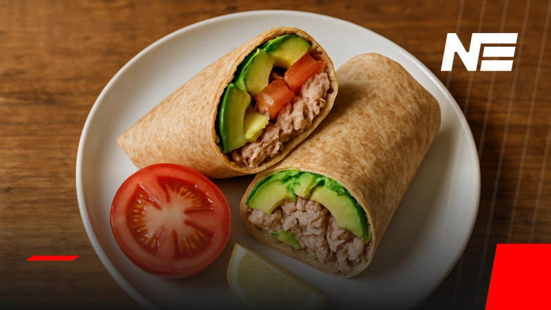 Wrap integral de atún con palta y tomate cortado al medio sobre plato blanco en mesa de madera