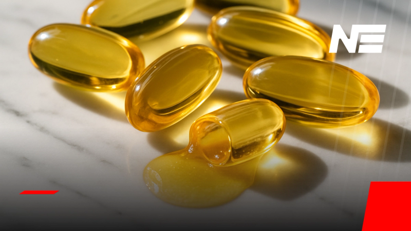 Cápsulas de omega-3 de aceite de pescado en primer plano sobre superficie de mármol blanco, una de ellas abierta mostrando el aceite dorado en su interior.