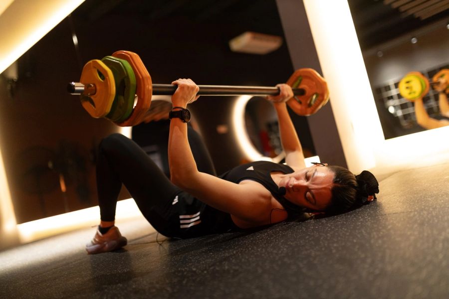 Alumna de Body Pump haciendo press de pecho con barra en el piso