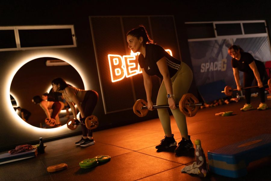 Alumna de Body Pump haciendo remo con barra frente al letrero BEATS