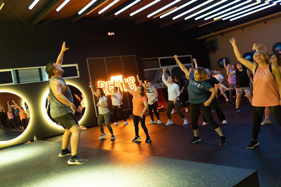 Profesor de Zumba guiando la coreografía con los brazos en alto