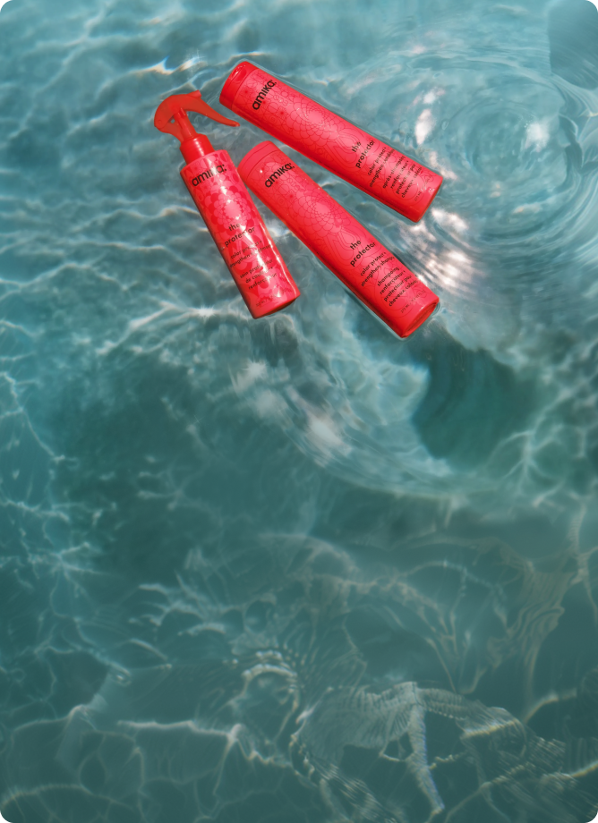 bottles of amika's the protector shampoo, conditioner, and treatment float in a swimming pool