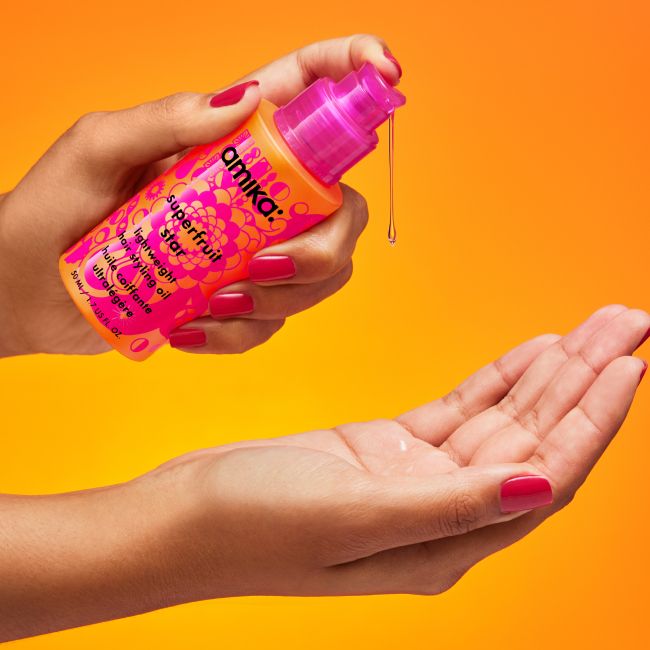 amika superfruit star hair oil dispensing from bottle into hand against orange background