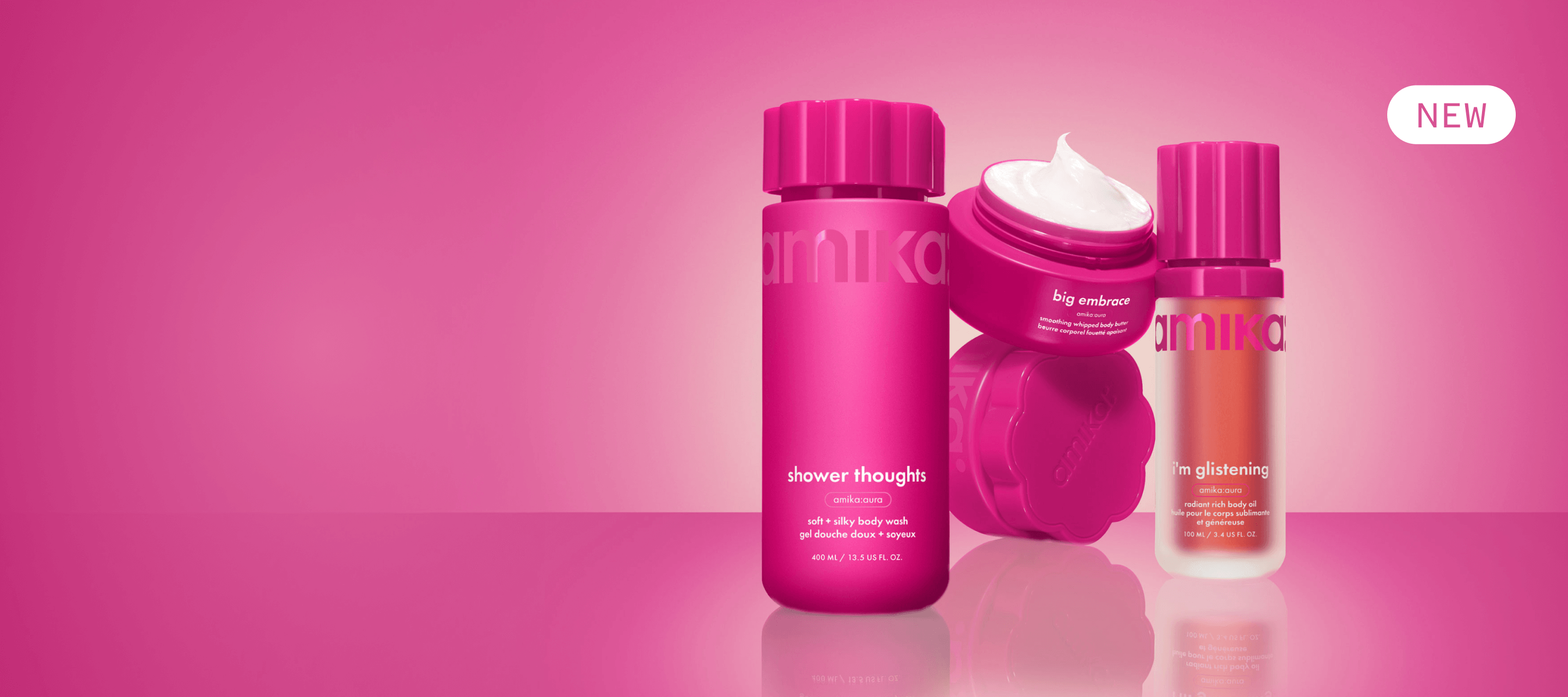 amika shower thoughts body wash, i'm glistening body oil, and big embrace body butter sit against a pink gradient background