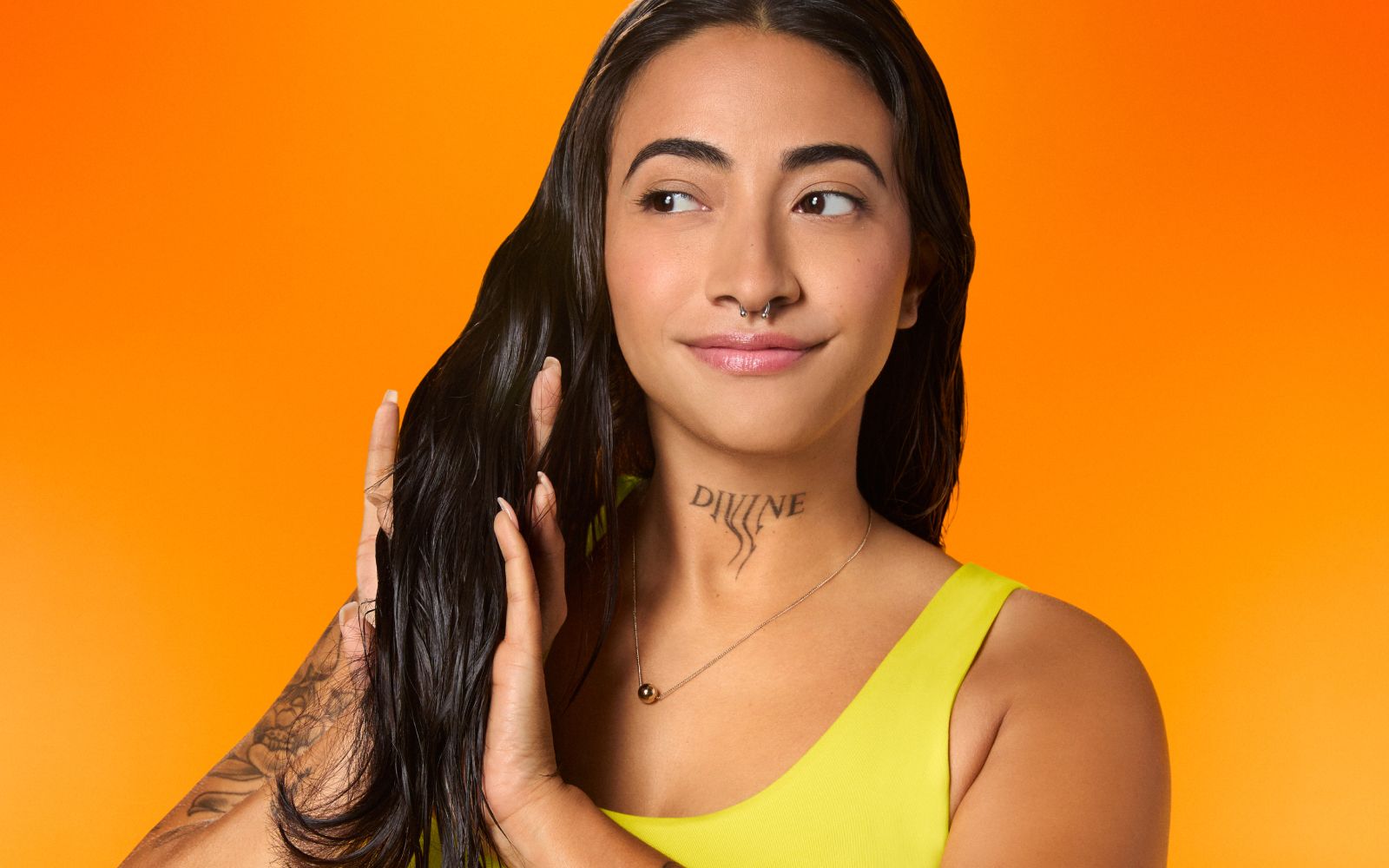 Showing dry hair application with superfruit star lightweight hair styling oil used on model Amber Perez shown in a bright yellow shirt, with dark hair, against an orange hued background