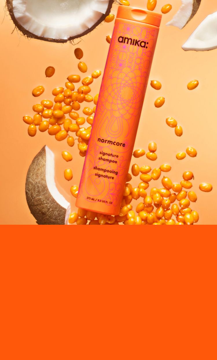 amika normcore signature shampoo surrounded by seabuckthorn and coconut ingredients on an orange background