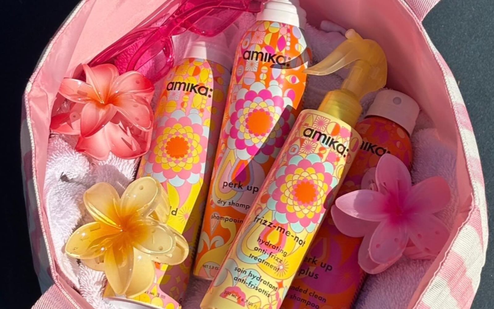 amika anti-frizz products lay in a pink bag with flower hair clips