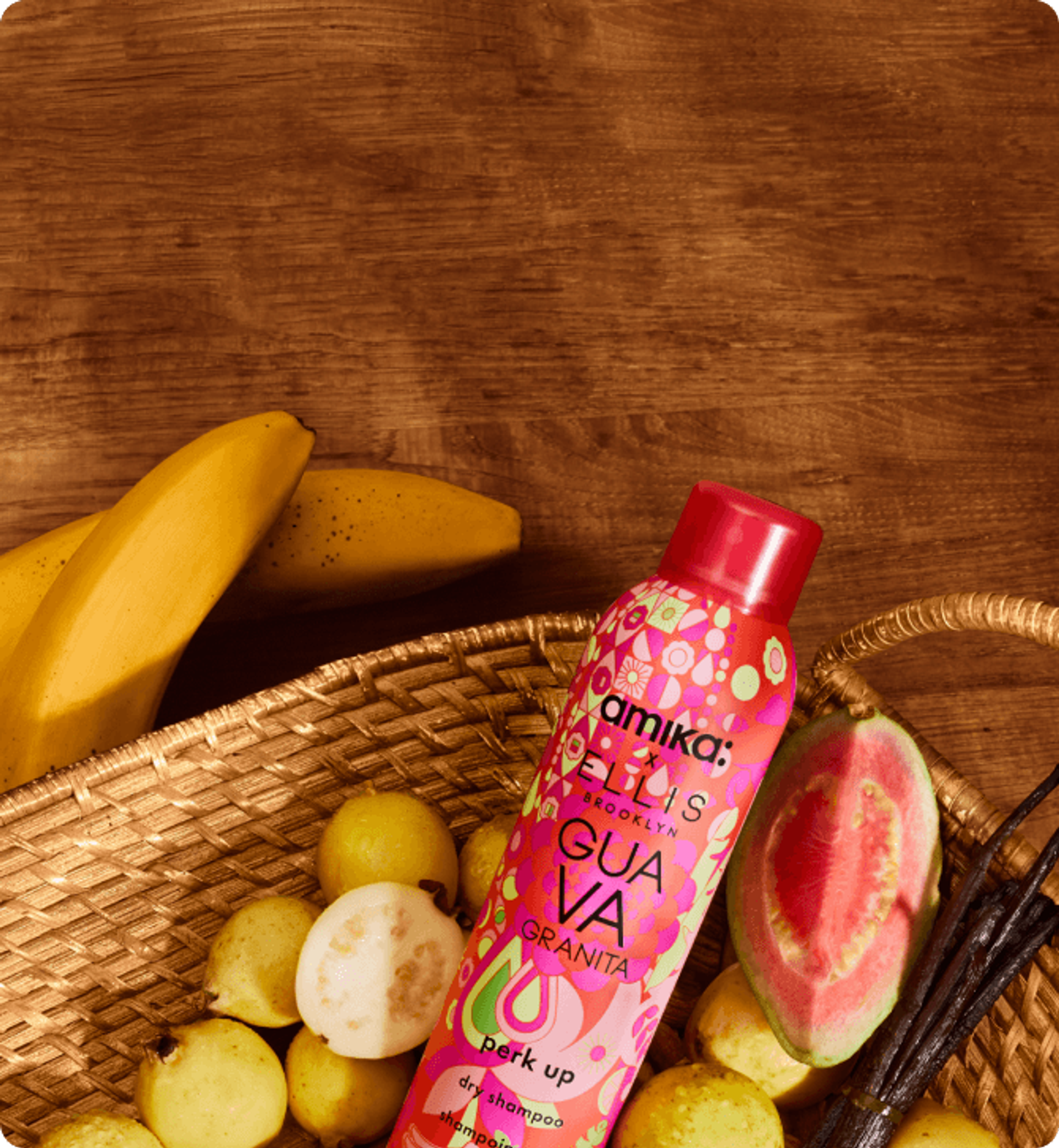 a bottle of amika perk up GUAVA GRANITA sits in a basket with guavas, bananas, and vanilla on a wooden background