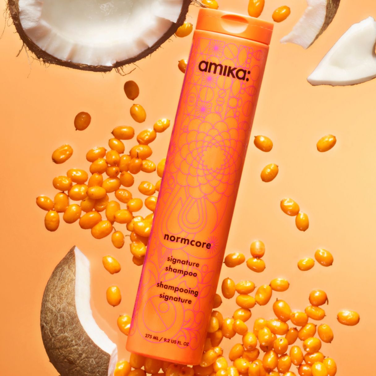 amika normcore signature shampoo surrounded by seabuckthorn and coconut ingredients on an orange background