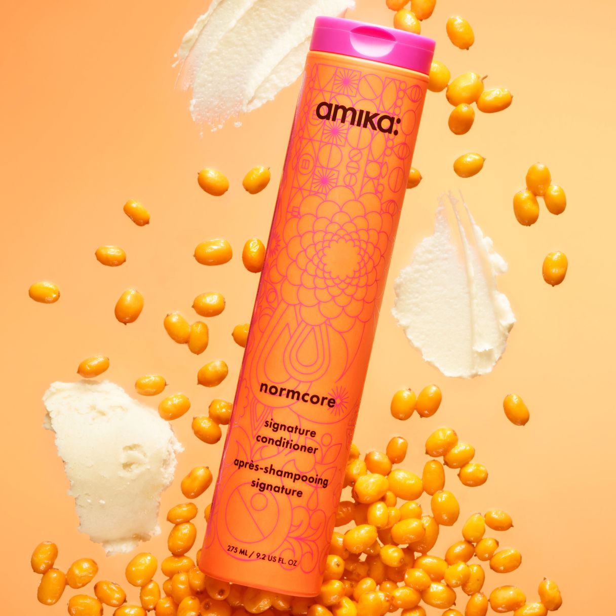 amika normcore signature conditioner surrounded by seabuckthorn and shea butter on an orange background