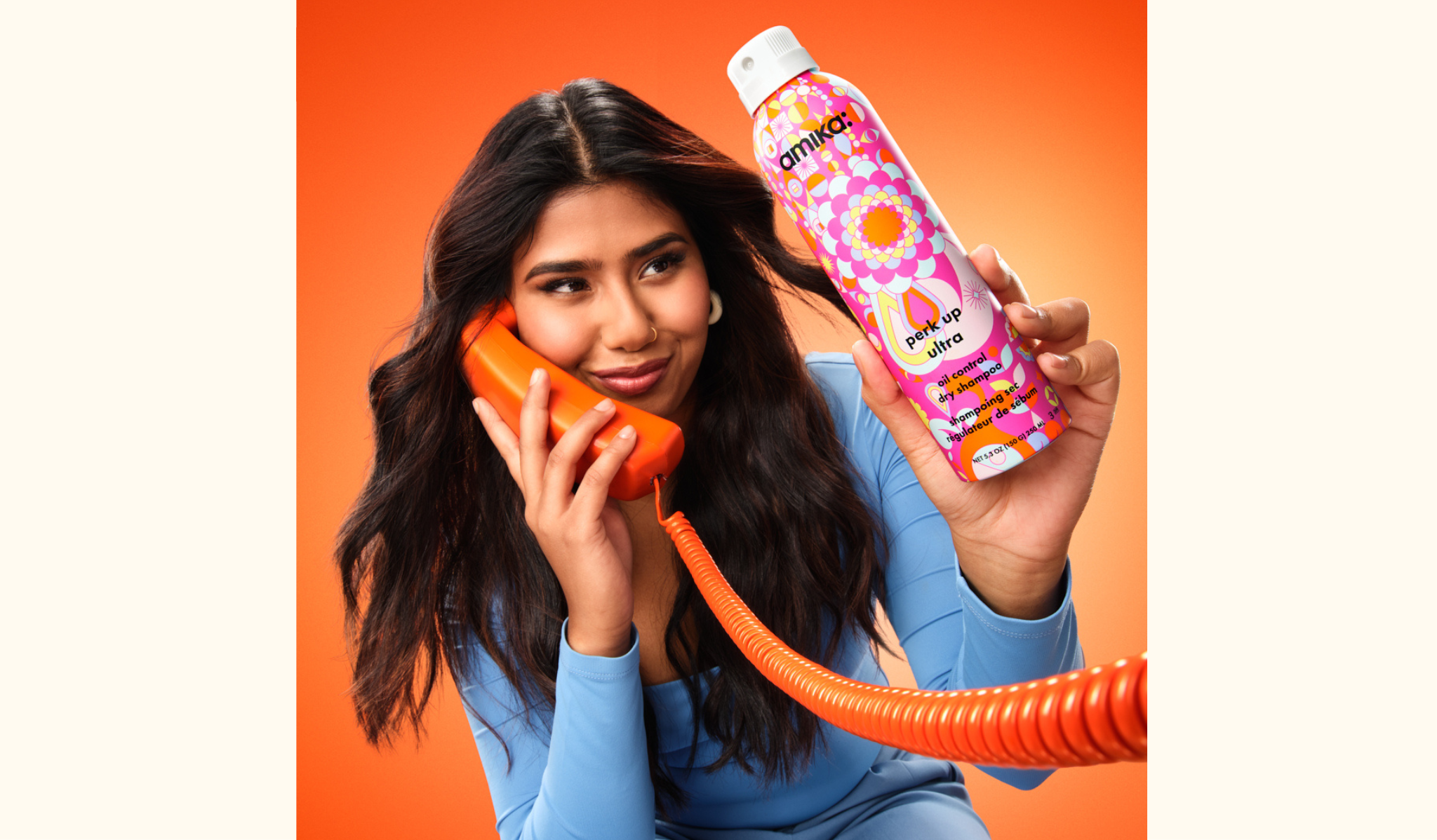 model with long, flowing hair holds amika's new perk up ultra oil control dry shampoo and a telephone