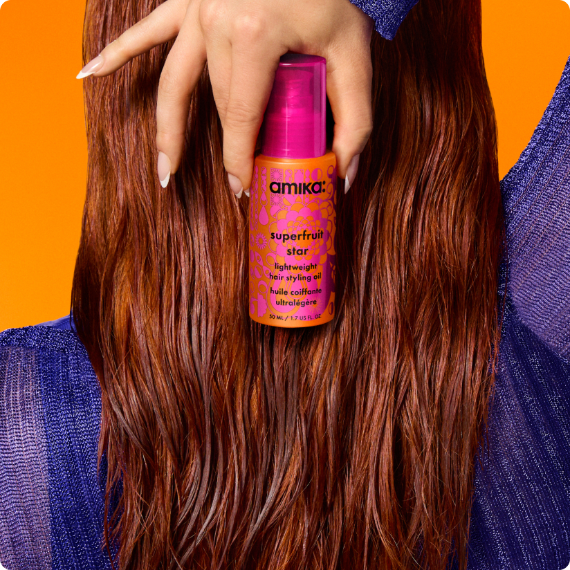 image shows a model holding a bottle of amika superfruit star oil behind their head.