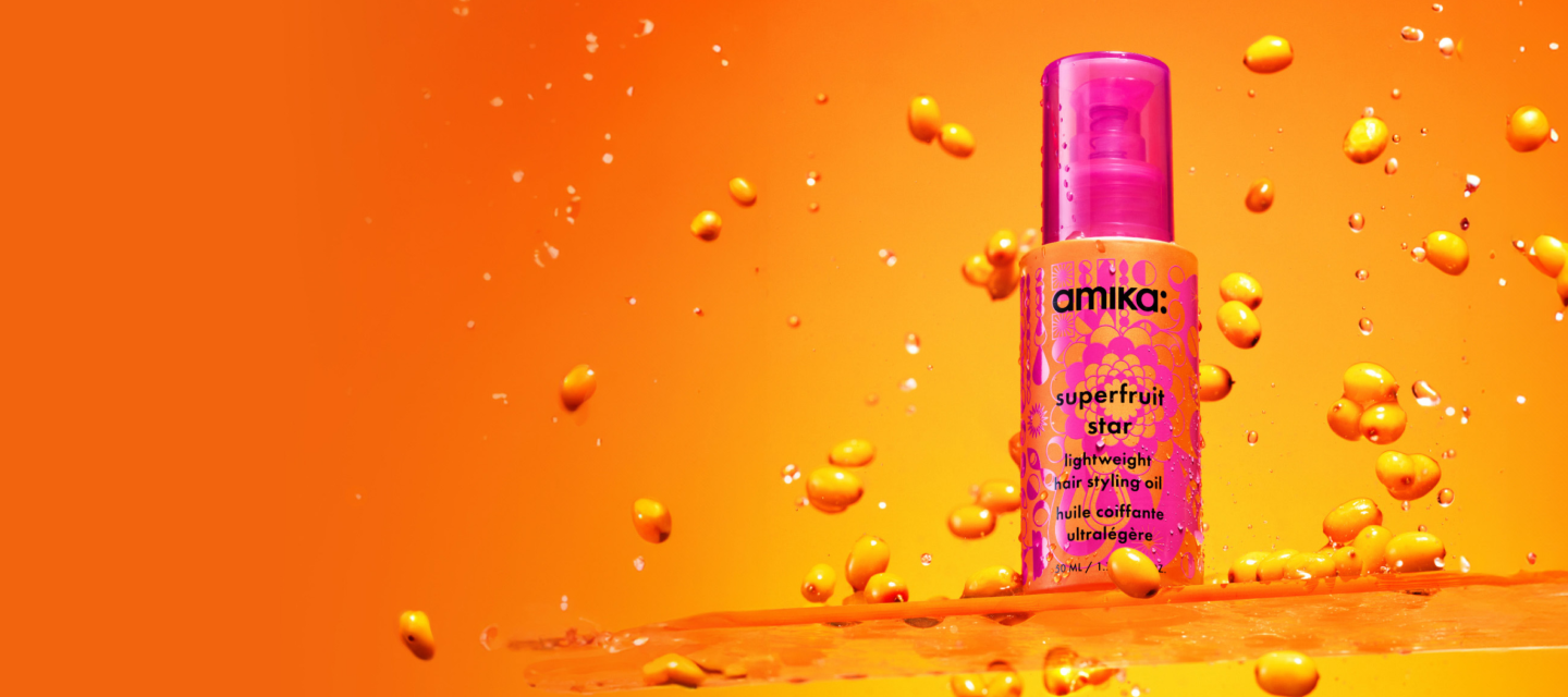 a pink and orange bottle of amika superfruit star lightweight hair styling oil surrounded by sea buckthorn berries