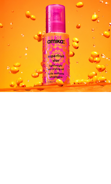 a pink and orange bottle of amika superfruit star lightweight hair styling oil surrounded by sea buckthorn berries