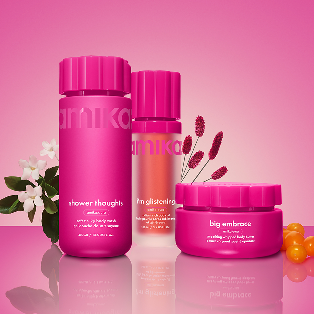 amika shower thoughts body wash, i'm glistening body oil, and big embrace body butter sit against a pink gradient background with flowers and sea buckthorn berries