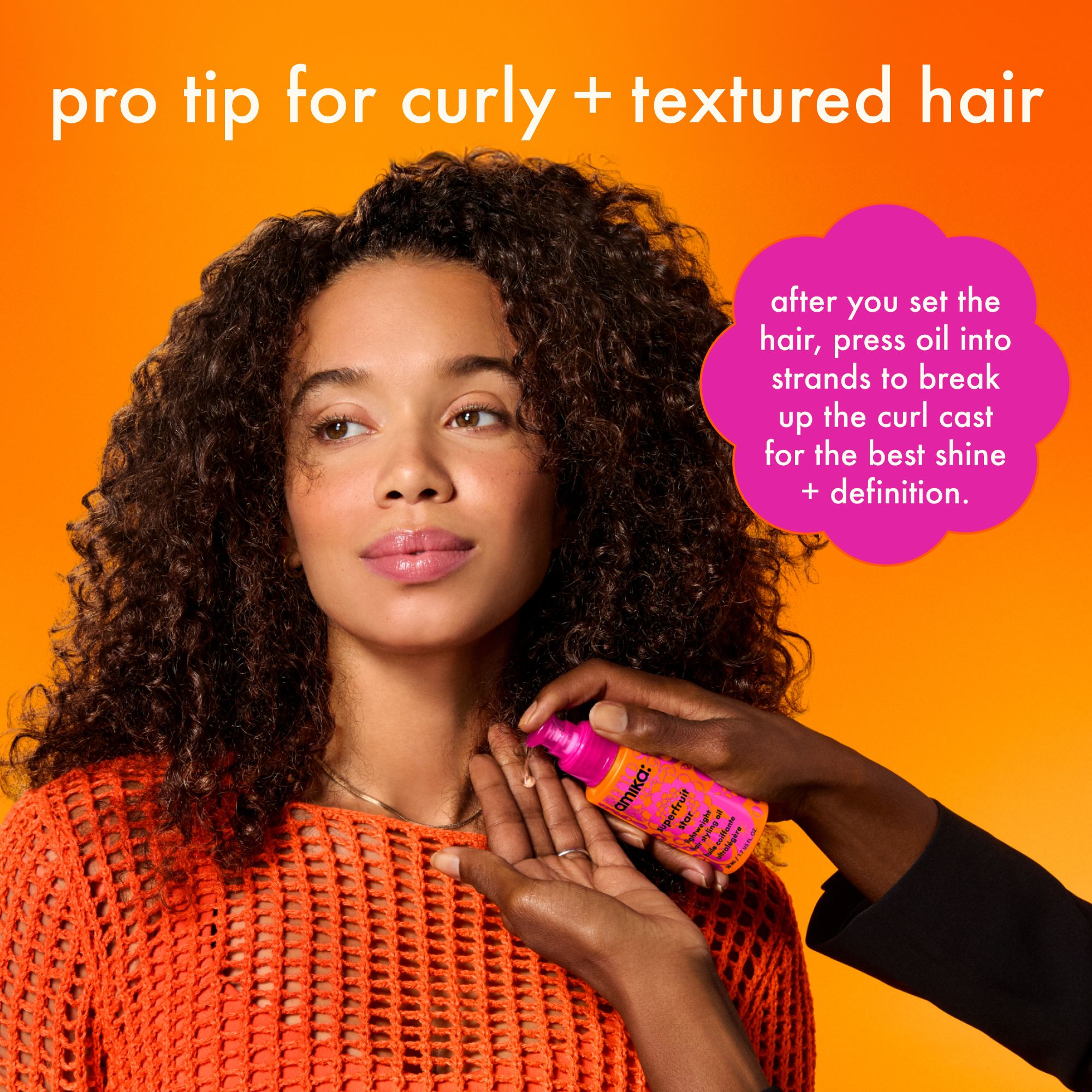 a model with curly hair stands while a stlyist holds amika superfruit star in their hands, about to apply the oil to the model's hair. Text reads: "Pro tip for curly + textured hair: after you set the hair, press oil into strands to break up the curl cast for the best shine + definition."