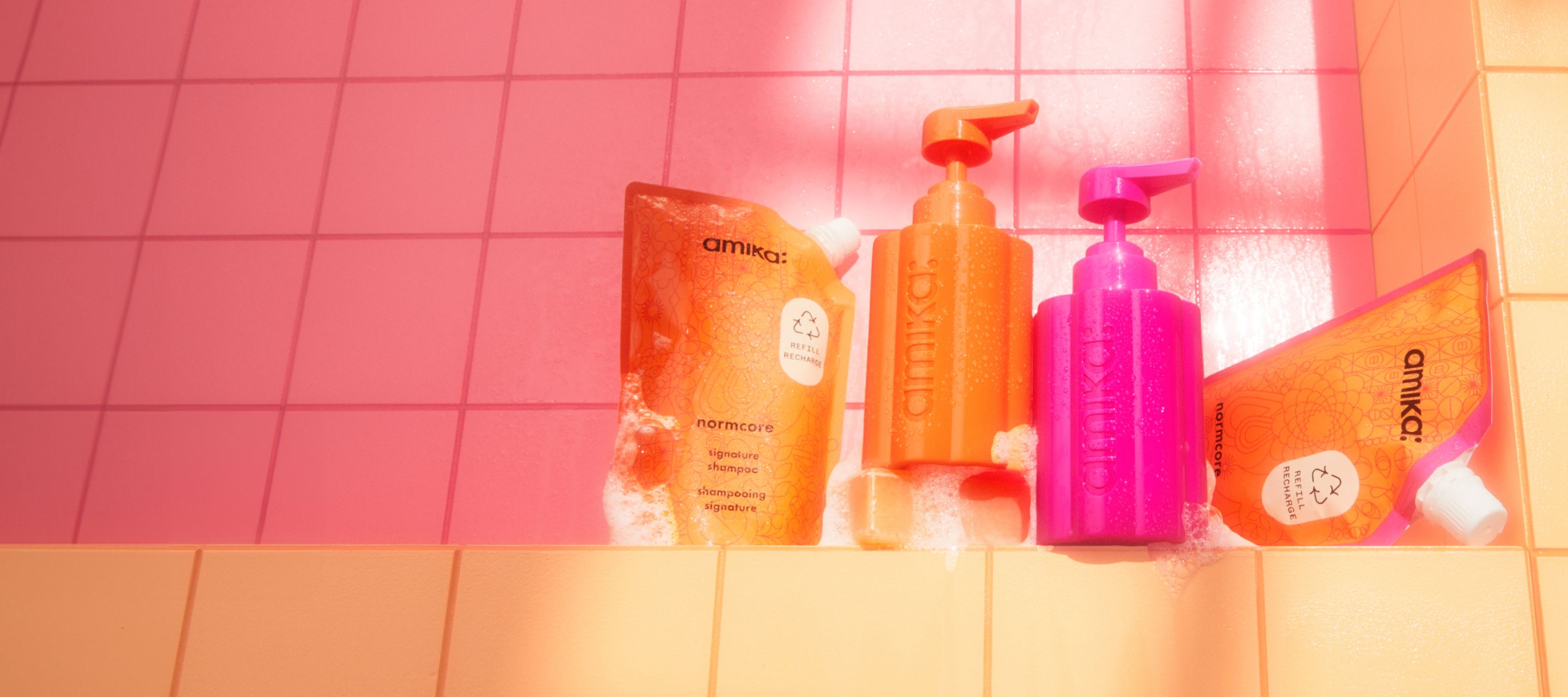 amika normcore shampoo and conditioner 500ml refill pouches with the forever friend refillable bottles on a pink and orange tile background