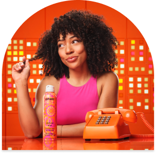 model with coily hair sits behind a telephone and amika new perk up plus extended clean dry shampoo spray bottle in 5.3 oz size