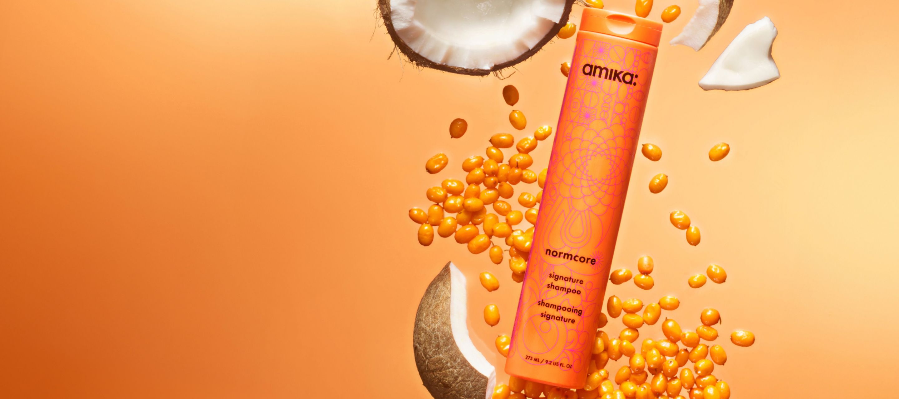 amika normcore signature shampoo surrounded by seabuckthorn and coconut ingredients on an orange background