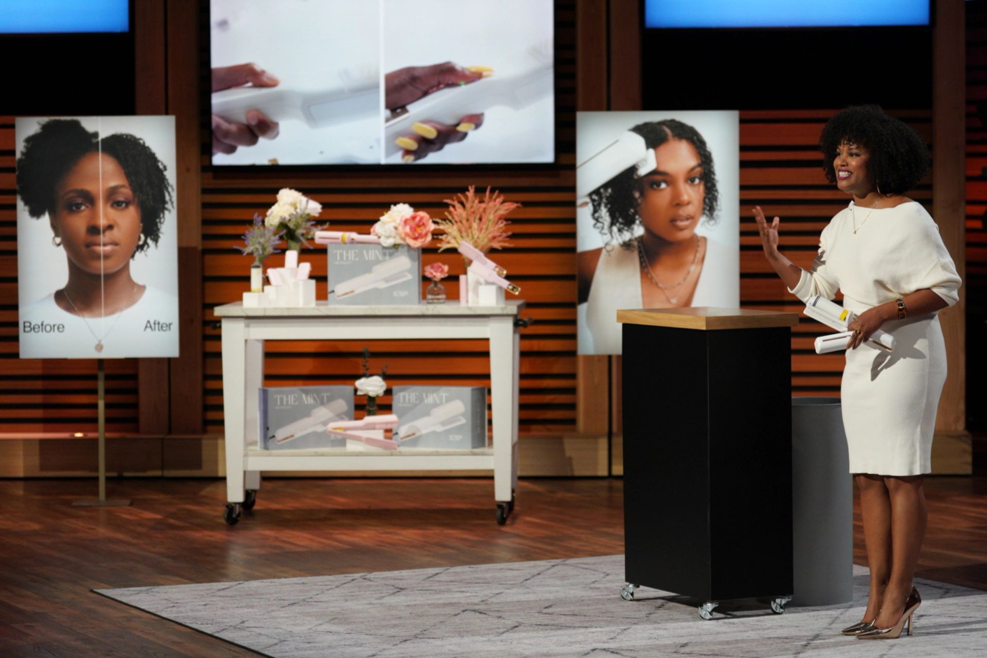 a person holding a hair tool stands on a stage speaking