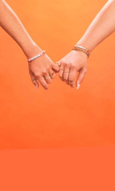 two amika models holding pinky fingers together on an orange background