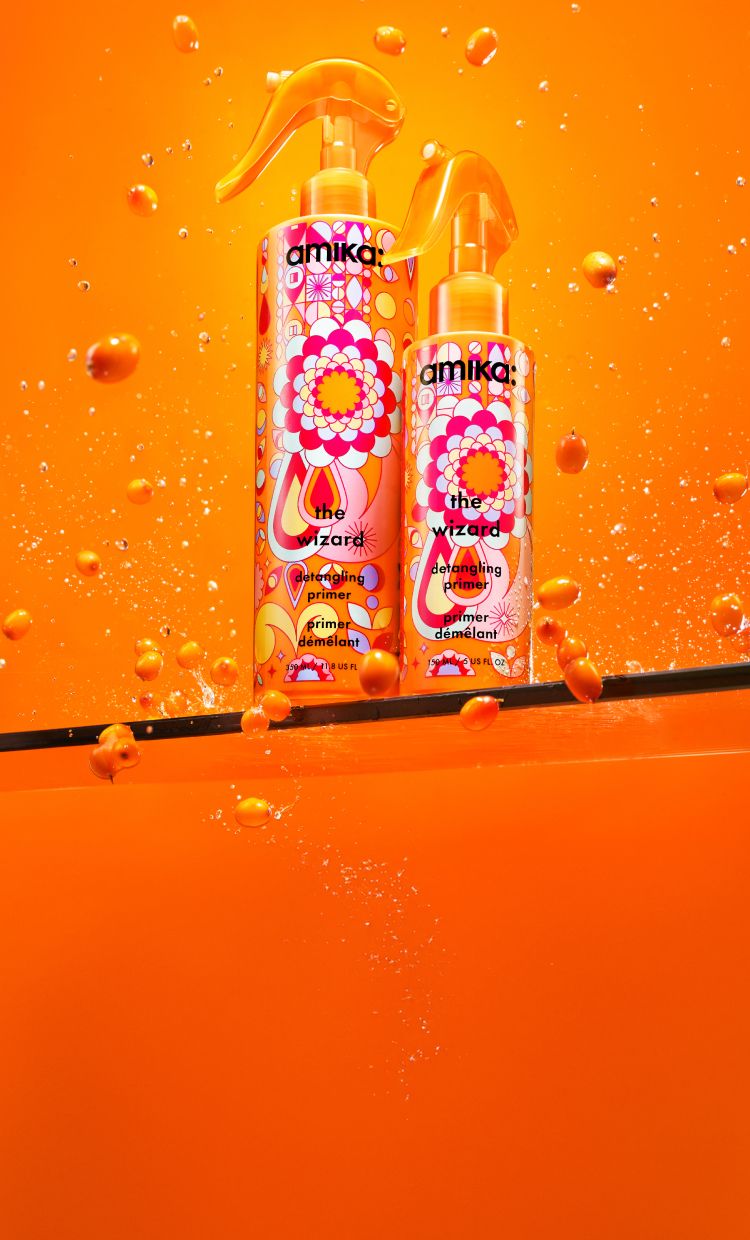 two bottles of the wizard detangling primer on a shelf with an orange background and seabuckthorn surrounding the bottles