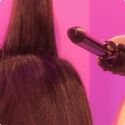 a GIF (moving image) of a hair stylist using an amika curling iron to add volume at the root and a light curl to a model's long brown hair