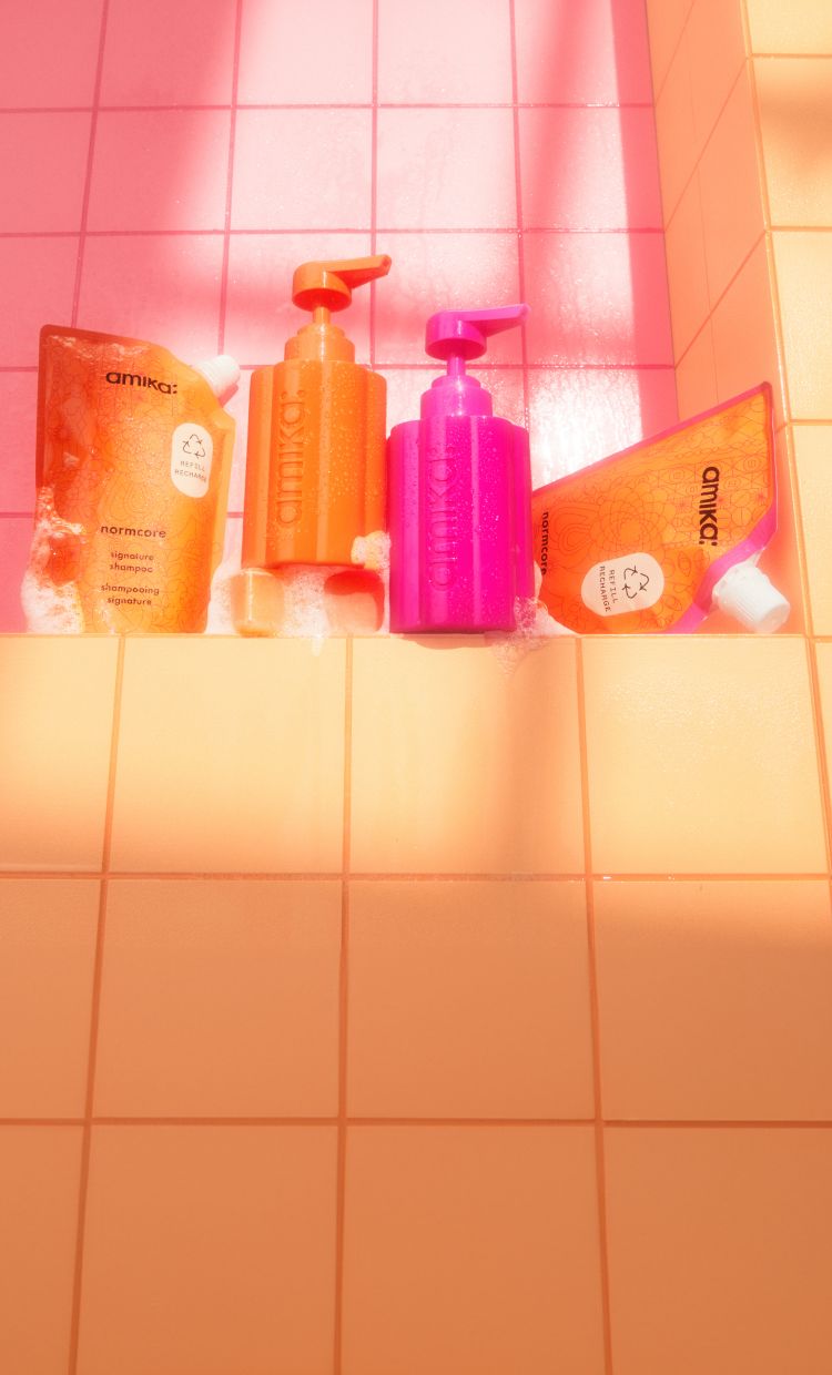 amika normcore shampoo and conditioner 500ml refill pouches with the forever friend refillable bottles on a pink and orange tile background