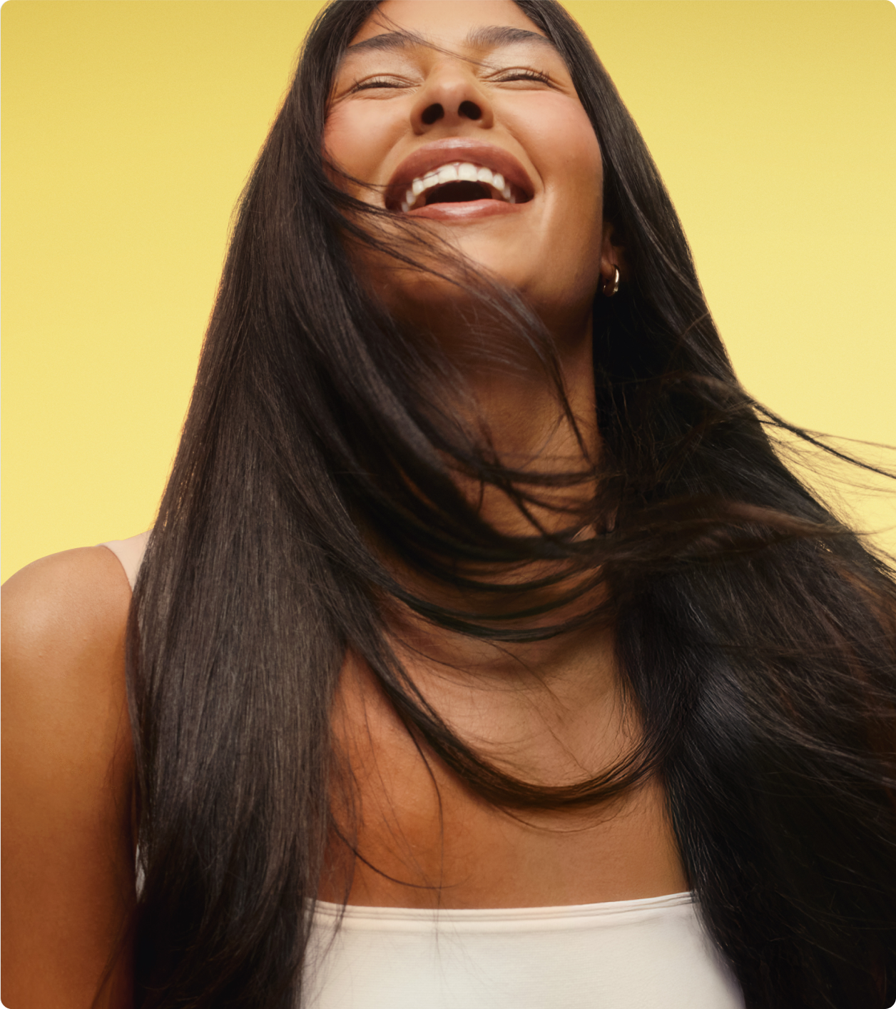 a model with smooth, dark hair smiles posing against a yellow background