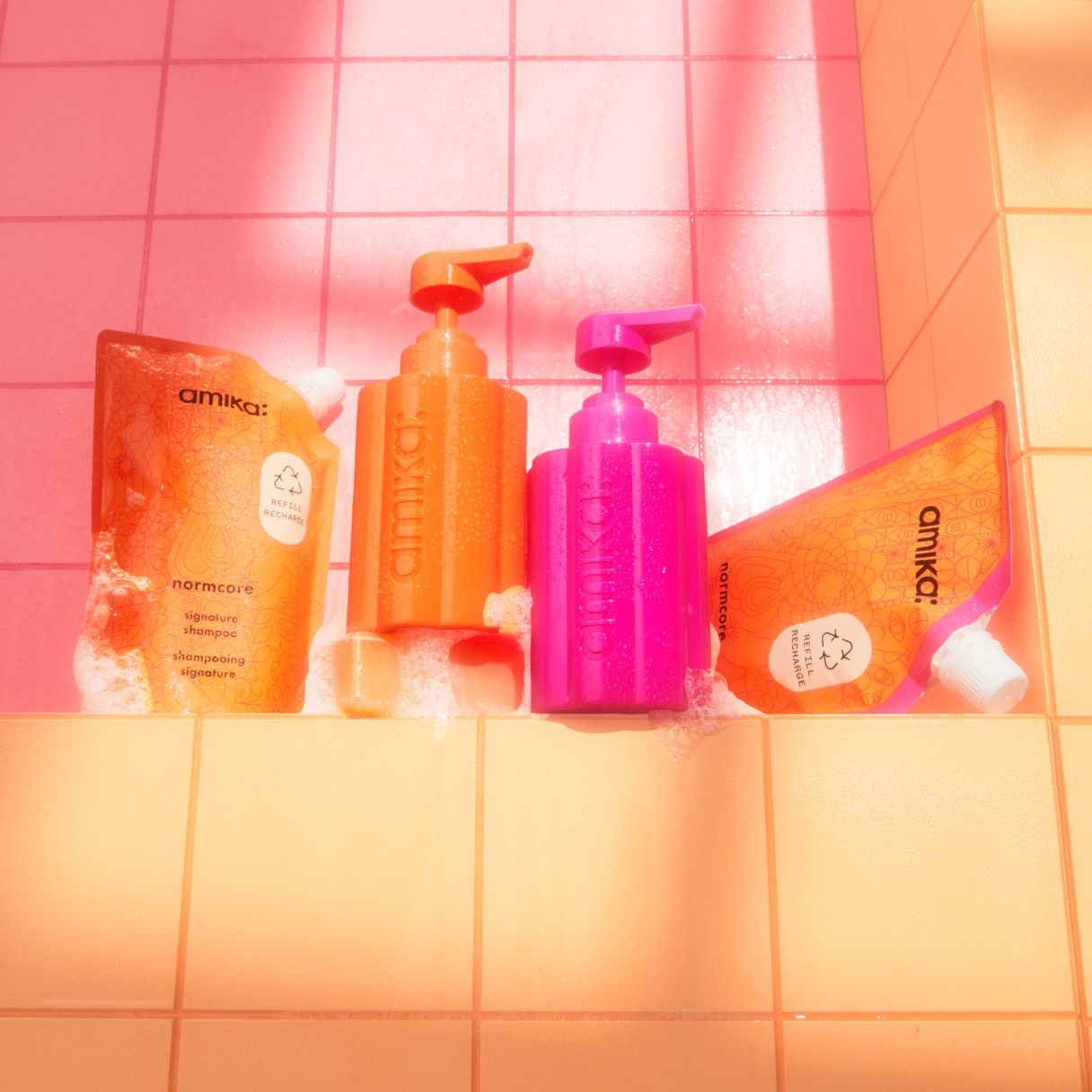 amika normcore shampoo and conditioner 500ml refill pouches with the forever friend refillable bottles on a pink and orange tile background