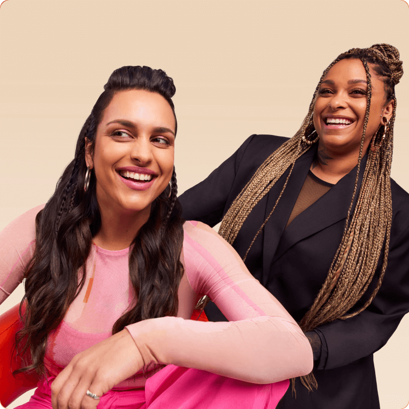 a stylist and her client in a chair smiling against a cream background