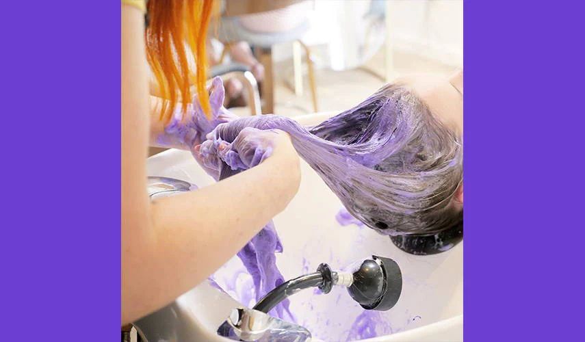 person's hair being washed with purple shampoo in hair salon