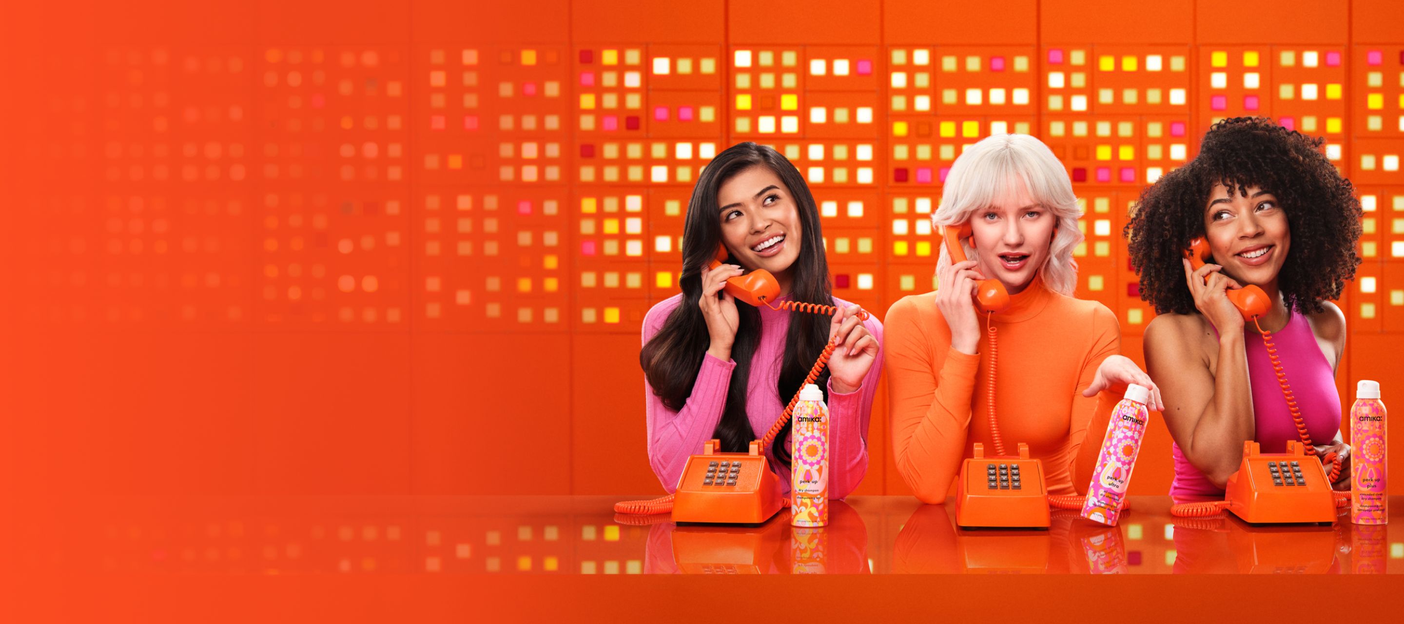 3 models talk on telephones and display amika perk up talc-free dry shampoo, perk up ultra oil control dry shampoo, and perk up plus extended clean dry shampoo.