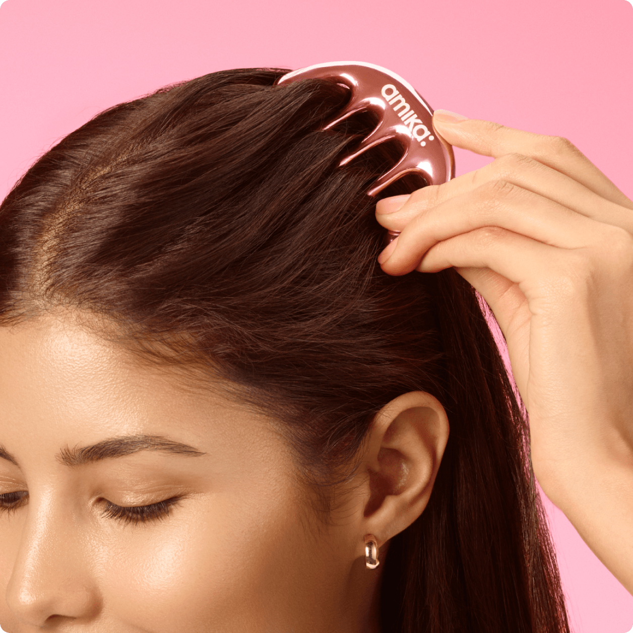 a model runs a scalp gua sha massager through their hair against a pink background