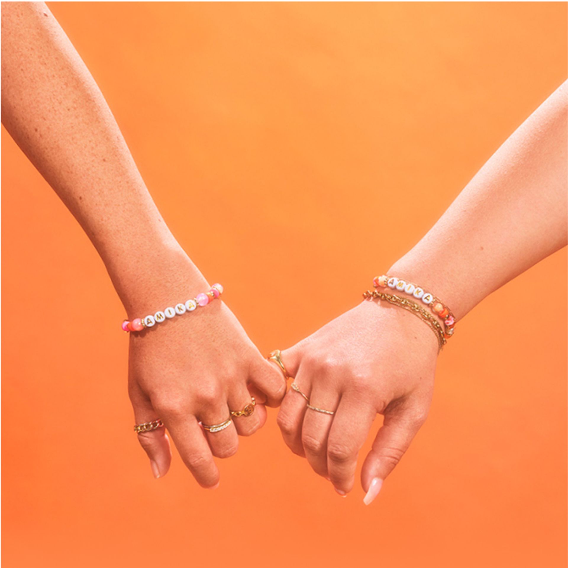 two amika models holding pinky fingers together on an orange background