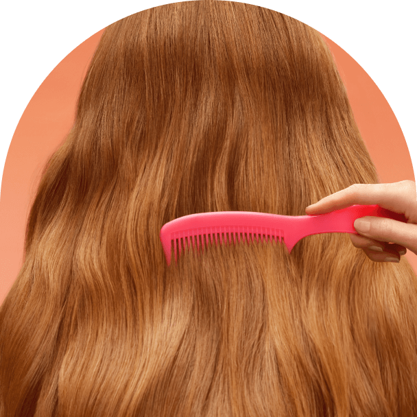 a pink comb moves through reddish hair against a pinkish-orange background