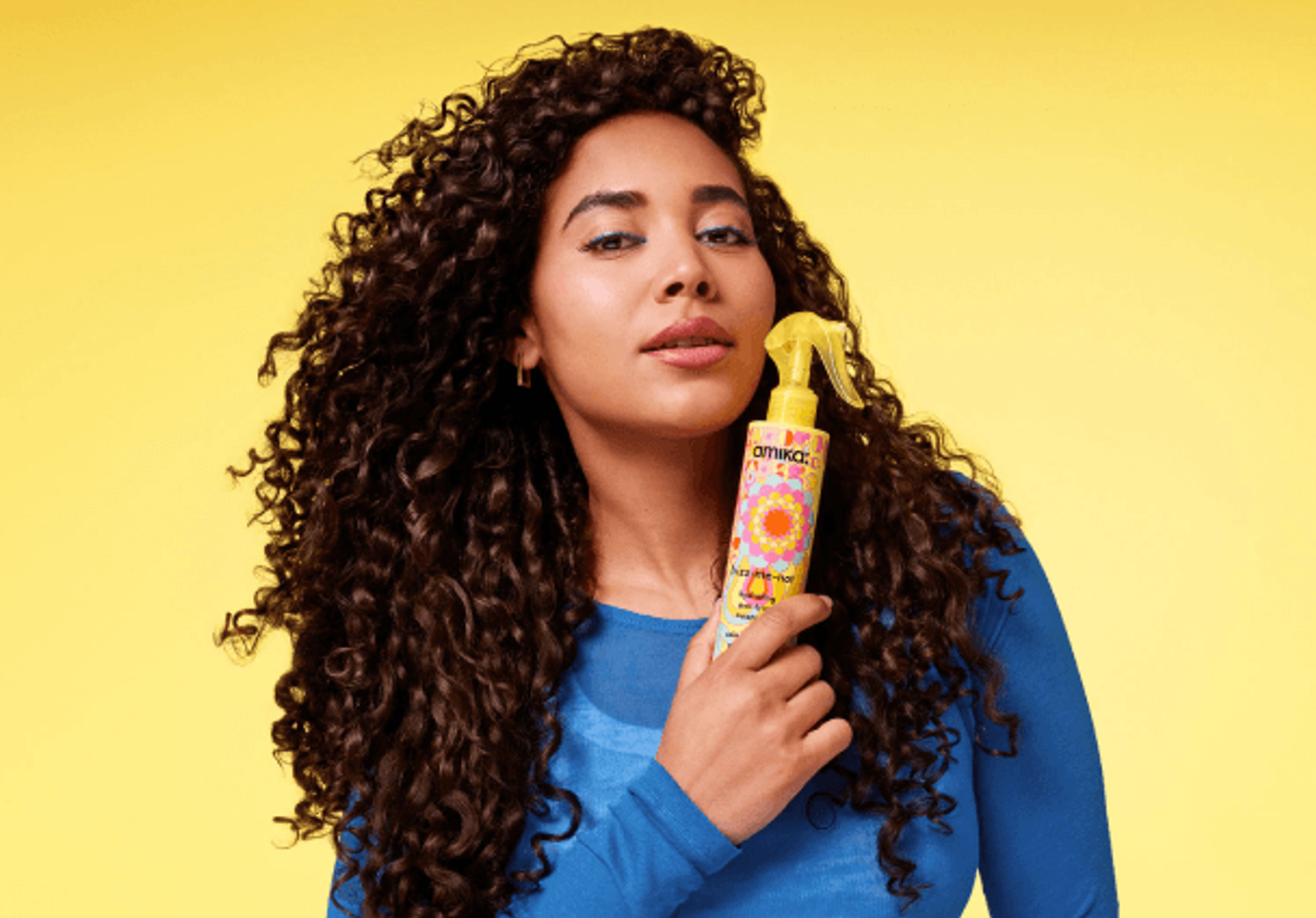 a model holds a bottle of amika frizz-me-not treatment