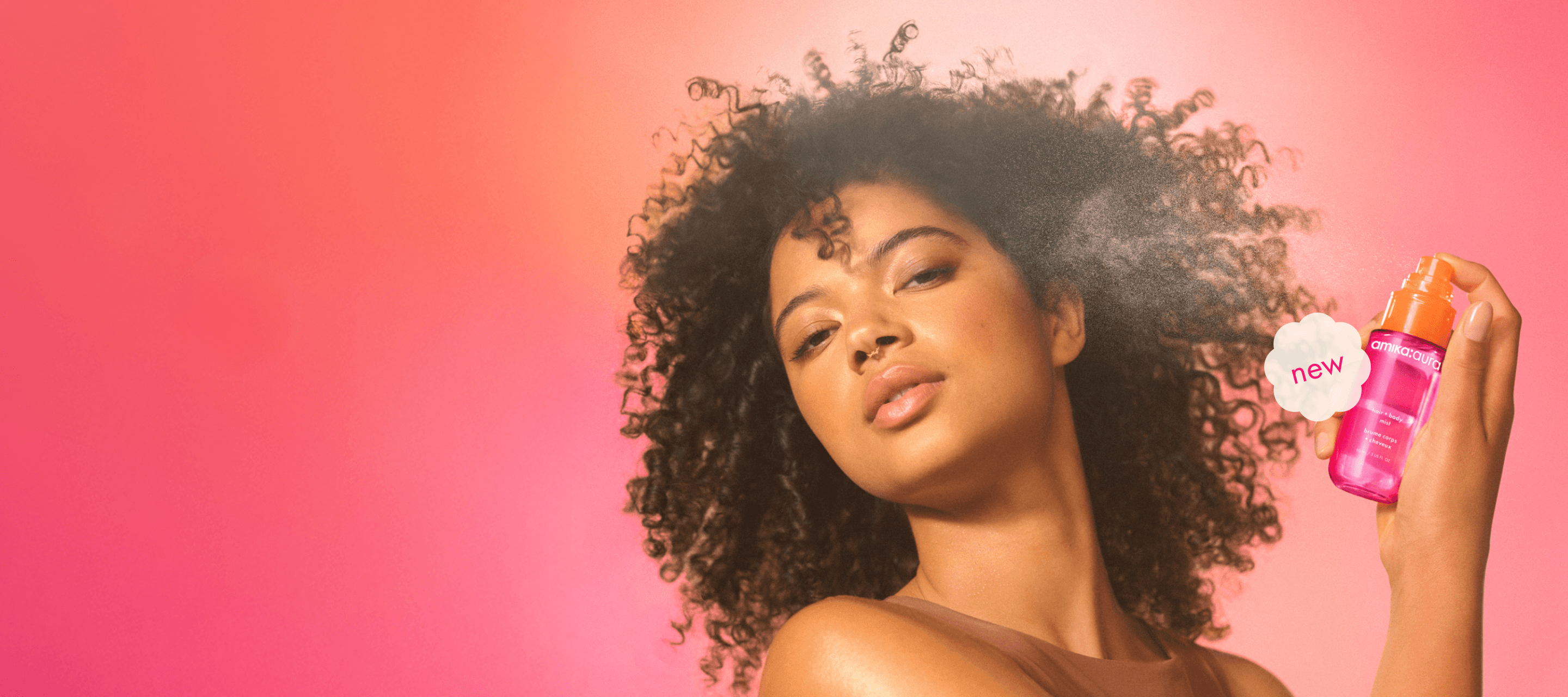 image of a model using aura mist on their skin against a pink orange gradient background.
