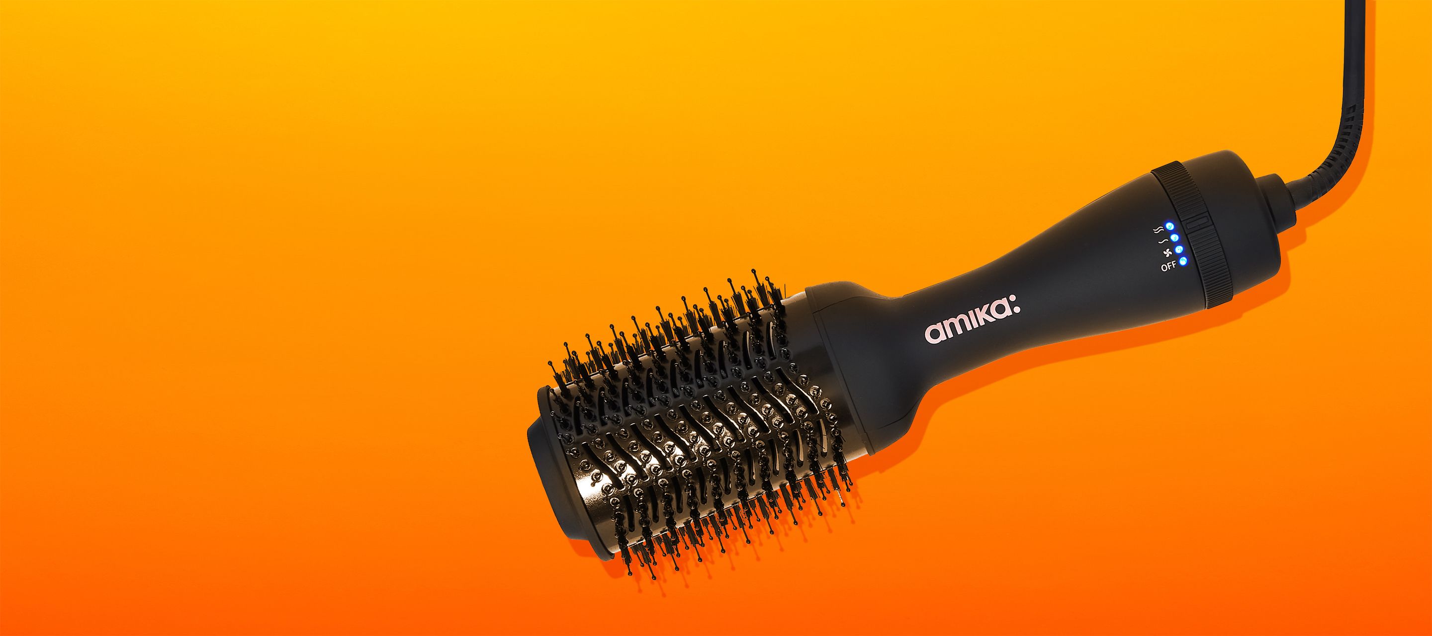 amika hair blow dryer brush 2.0 on an orange and yellow background