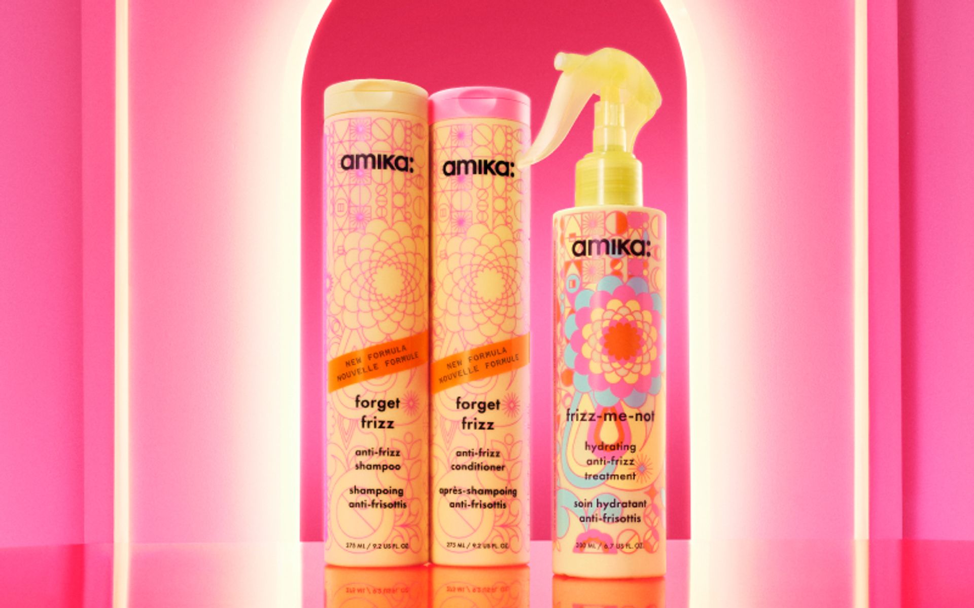 Image of amika frizz collection against a pink backlit background. Products featured include forget frizz shampoo and conditioner alongside the frizz-me-not treatment.