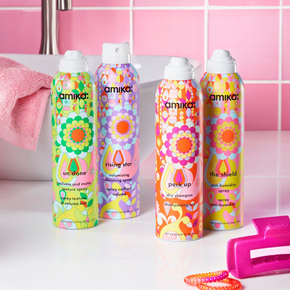 amika un.done volume and matter texture spray, rising star volumizing finishing spray, perk up dry shampoo and the shield ant-humidity spray full size products sitting in front of a white sink with a pink tile background