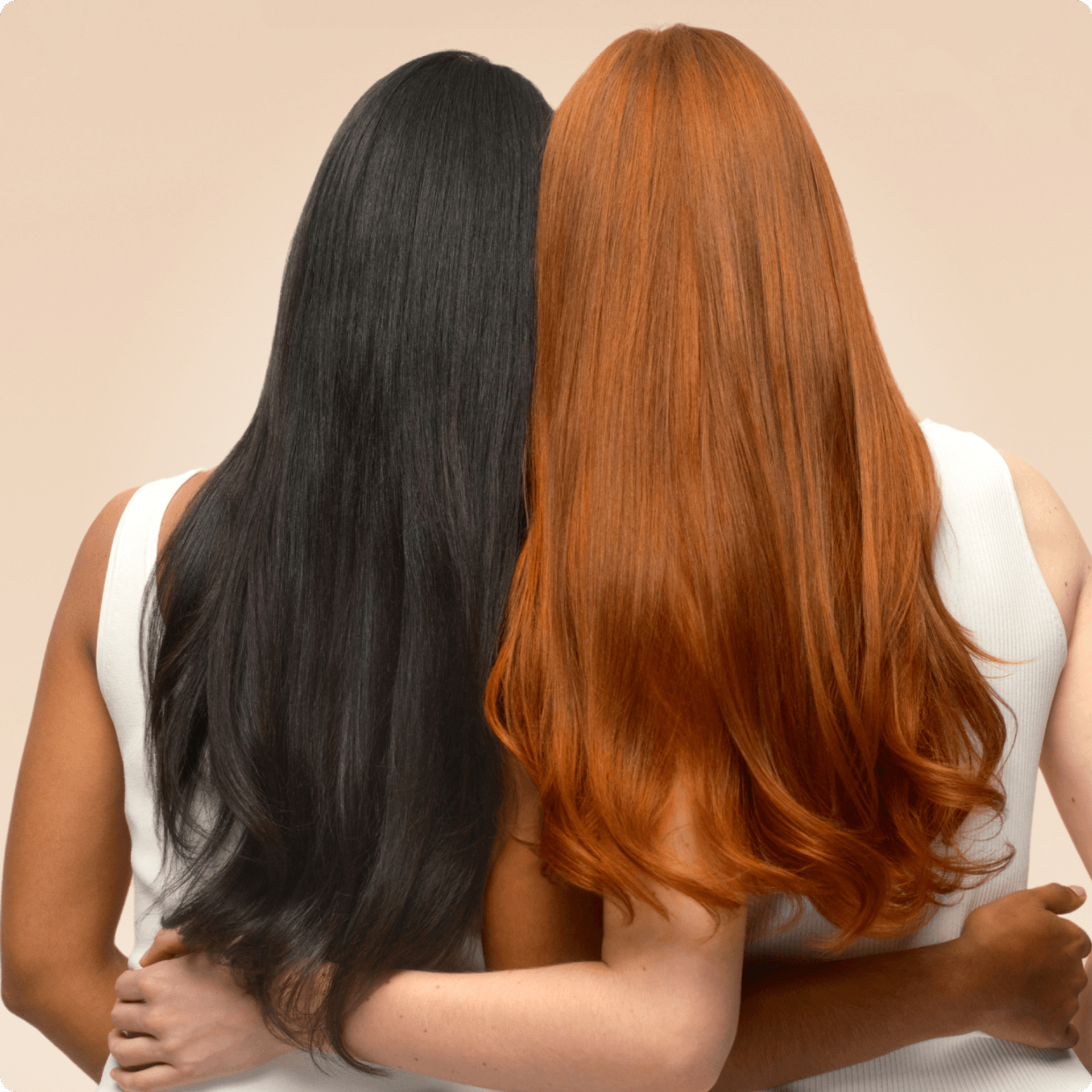 a model with long, dark brown hair and model with long, red hair with their backs turned stand with their arms around each other