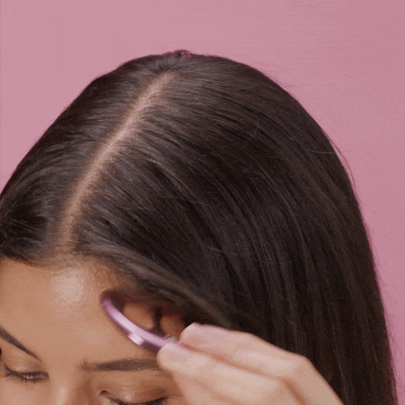 a gif of a model running a scalp gua sha massager through their hair against a pink background