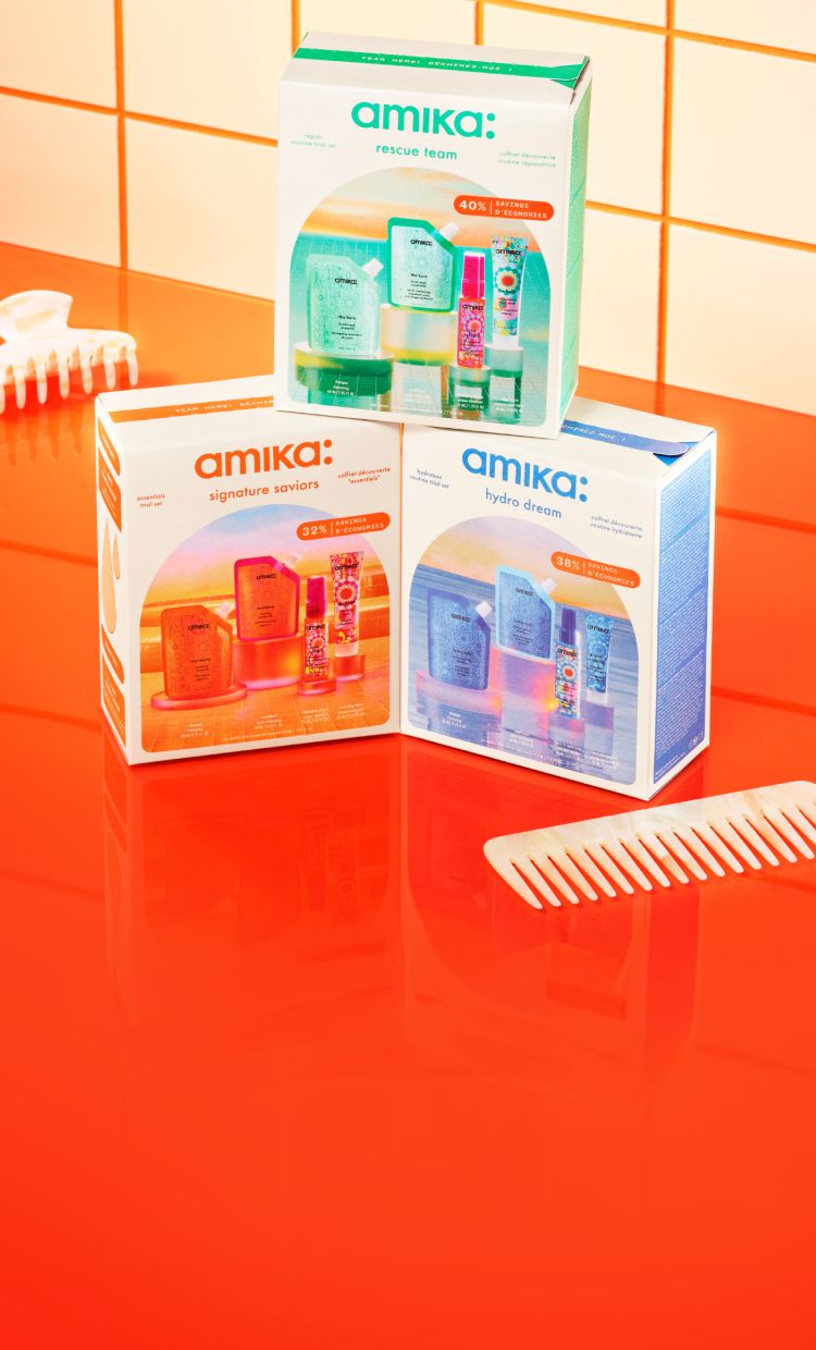 3 amika value sets stacked on top of an orange countertop surrounded by a white clip and white comb