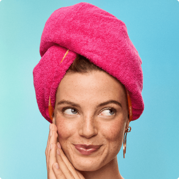 a model wears a hot pink towel on their head, wrapped around their hair against a blue background