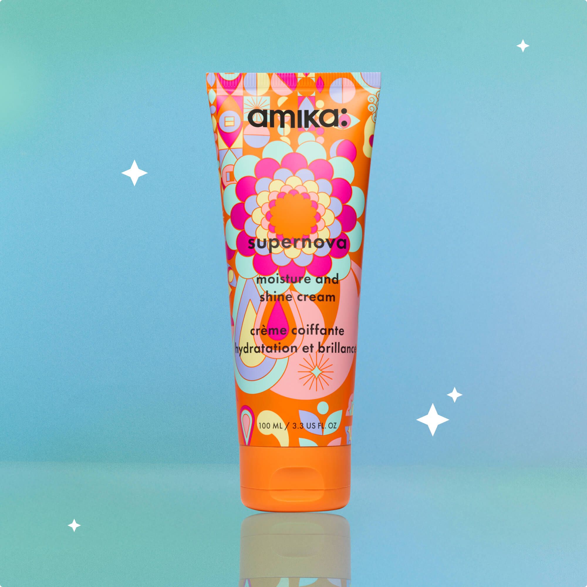 a tube of amika supernova moisture and shine cream sits against a bluish-green background with small white stars