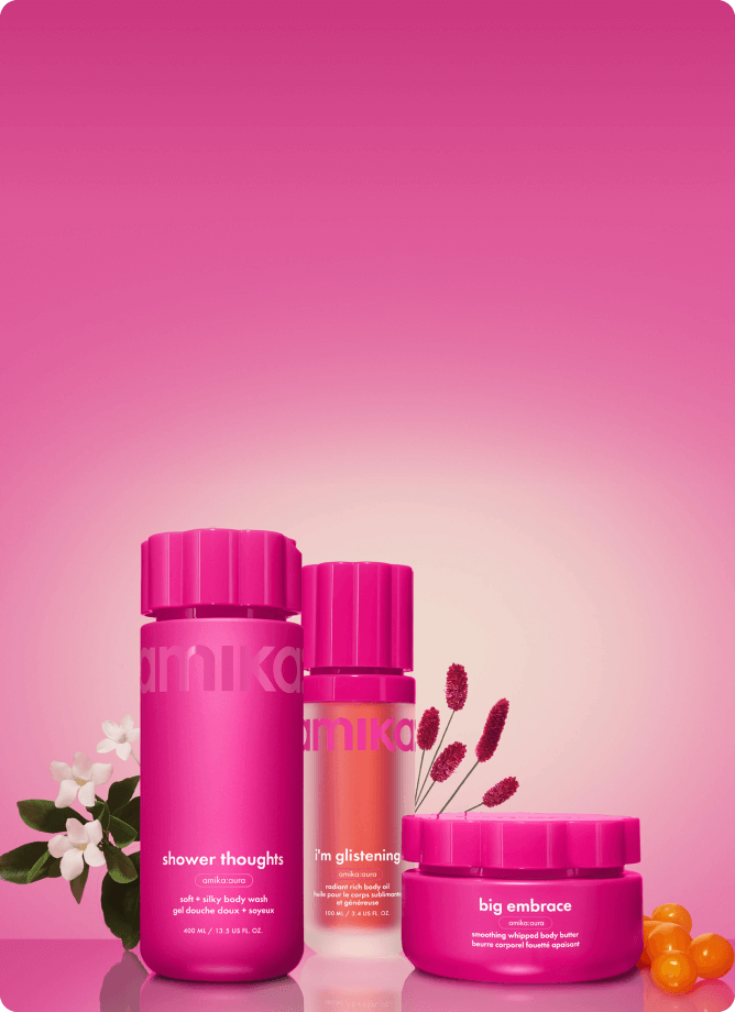 amika shower thoughts body wash, i'm glistening body oil, and big embrace body butter sit against a pink gradient background with flowers and sea buckthorn berries